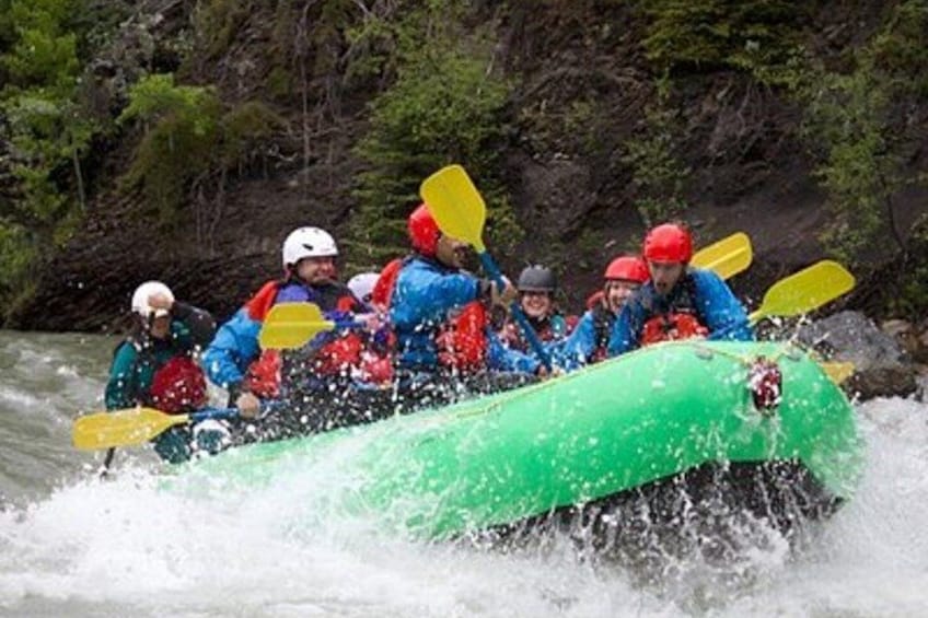 A group of people in a green raft navigating a river. 2