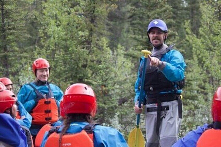 A group of people in outdoor gear, including helmets and life jackets, in a forested area. 5