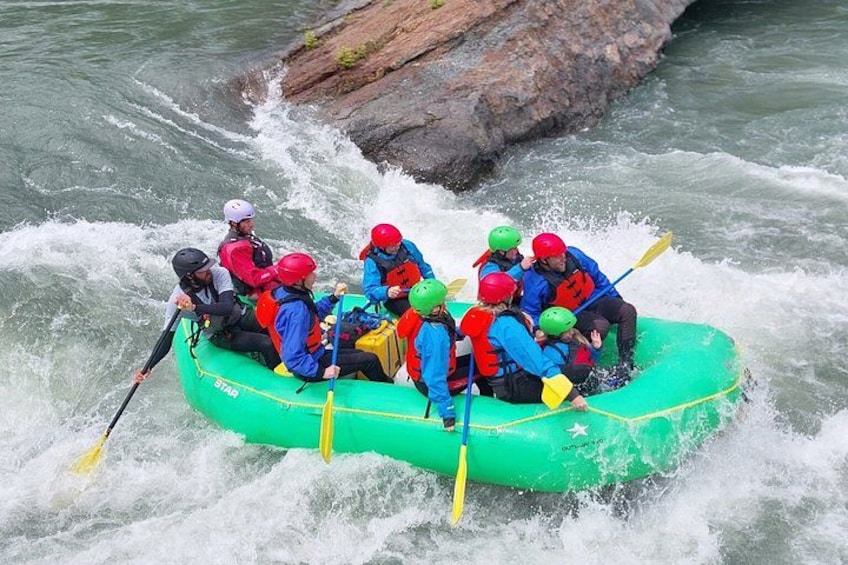 A group of people in a green raft navigating through a river with rapids. 4
