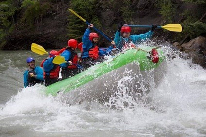 A group of people in a green raft navigating a river. 1
