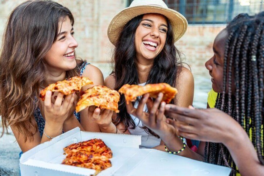 Three people sharing pizza at an outdoor table. 1