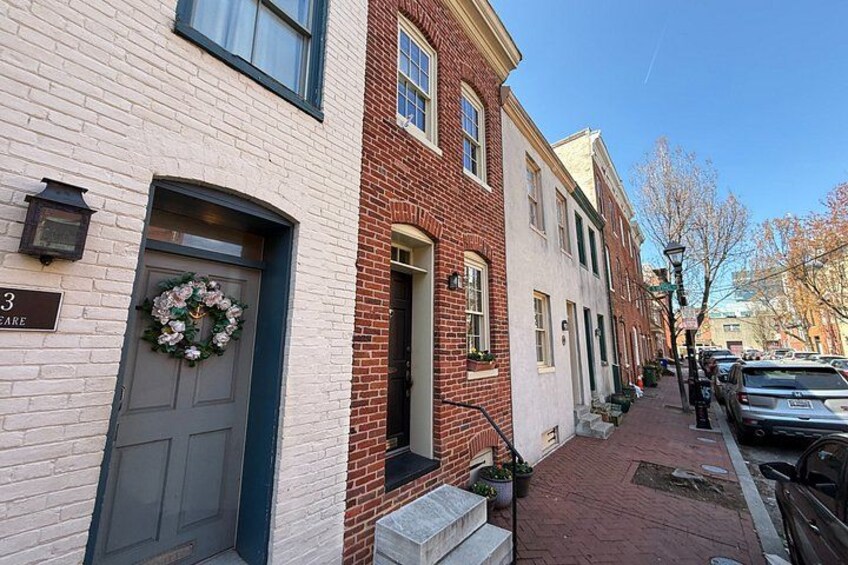 A brick building with a door, a street with parked cars, and a clear sky. 2