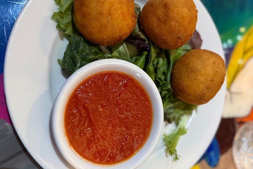 A plate with three golden-brown fried balls, a bowl of red sauce, and a side of green salad. 3