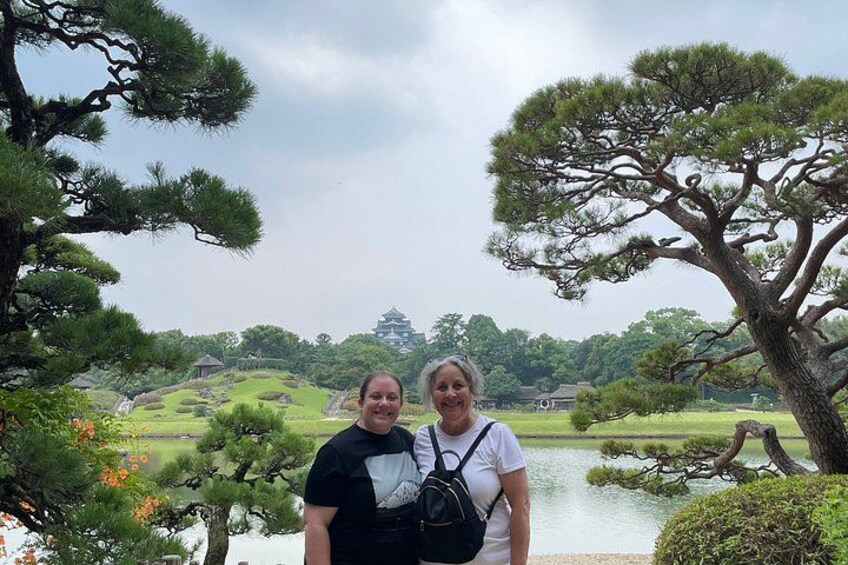 Two people standing in front of a pond with trees and a distant building. 4