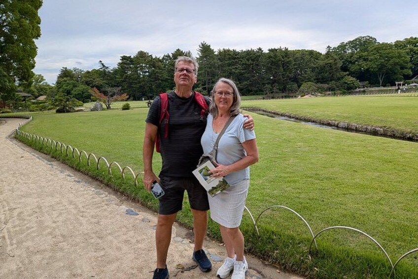 Two people standing on a path with a grassy field and trees in the background. 5