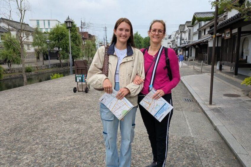 Two people standing on a cobblestone path with a canal and traditional buildings in the background. 2