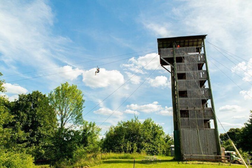 A tall, wooden tower with a platform at the top, surrounded by greenery and a clear sky. 1