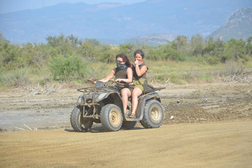 Two people on an off-road vehicle in a dry, open landscape with sparse vegetation and distant mountains. 5