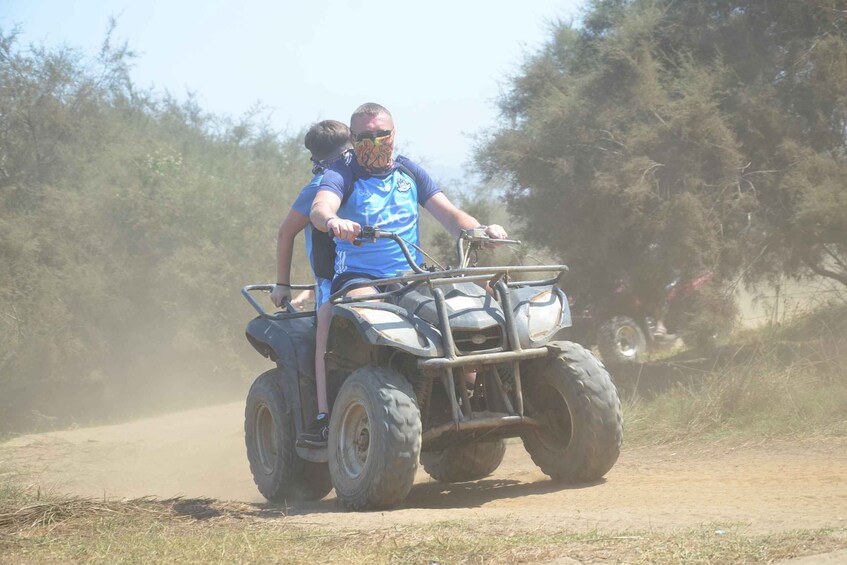 A person riding a quad bike on a dirt path surrounded by trees. 4
