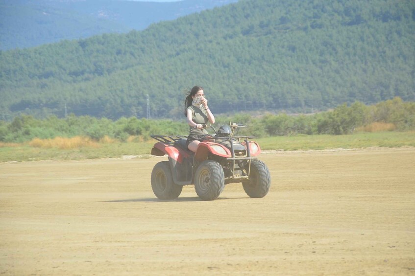 A person riding a red ATV on a dirt road with a forested hill in the background. 2