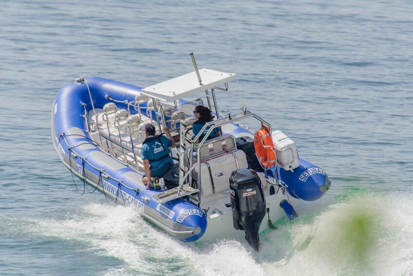 Een blauwe opblaasbare boot met twee personen, een motor en een oranje reddingsboei. 2