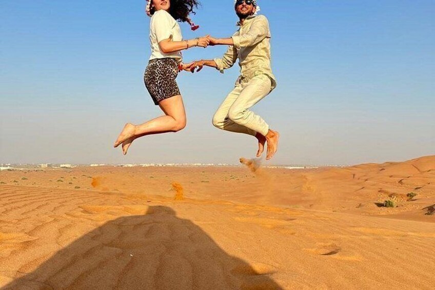 Two people jumping in a desert with sand dunes in the background. 2