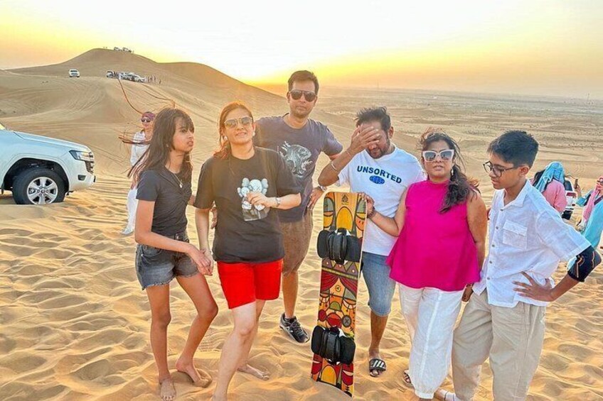 A group of people on a sandy beach with a dune in the background and a vehicle parked nearby. 5