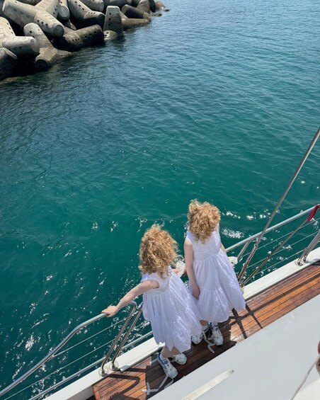 Zwei Kinder in weißen Kleidern stehen auf einem Bootsdeck und blicken auf das Wasser. 3