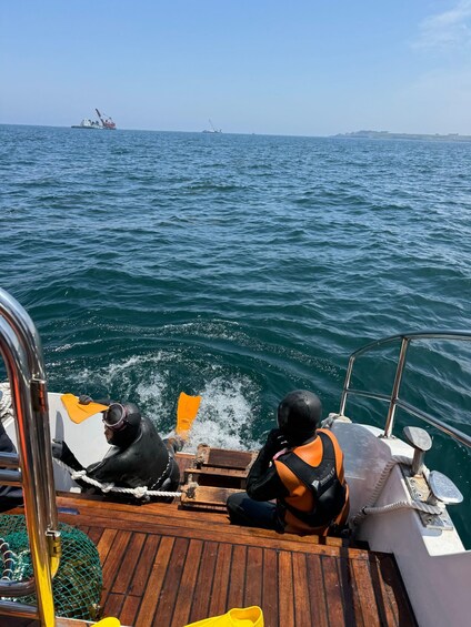 Two people on a boat, one wearing a diving mask and life jacket, with a ship in the background. 3