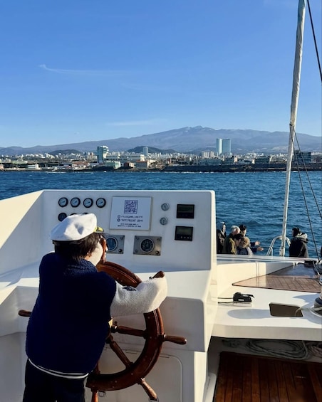 Eine Person steuert ein Boot, im Hintergrund sind Stadtansichten und Berge zu sehen. 5