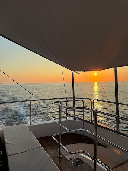 A boat deck at sunset with a view of the ocean and a distant ship. 2