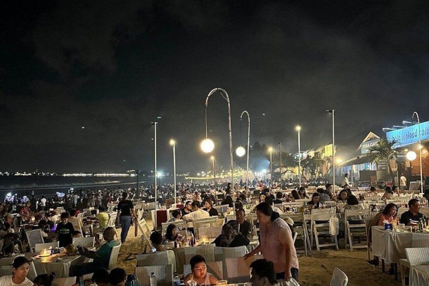 Un espace de restauration animé situé sur la plage, avec des tables et des chaises, des lampadaires et une vue lointaine sur la mer. 4