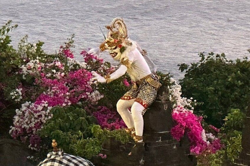 Une personne vêtue d’un costume traditionnel, assise sur un rocher, entourée de fleurs roses et blanches. 2