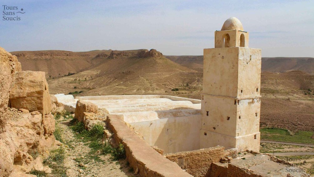 A desert landscape with ancient ruins, including a tower with a dome and arched windows. 2