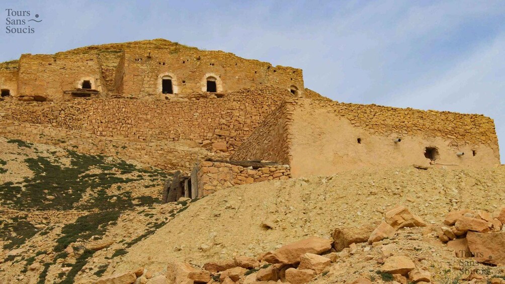 An ancient stone structure with multiple doorways and a steep, rocky hillside. 3