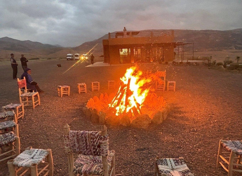 A campfire with chairs arranged in a circle, a building in the background, and mountains in the distance. 4