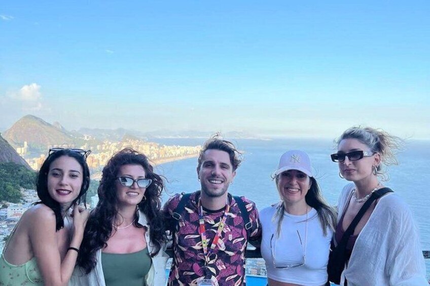 A group of people on a coastal overlook with a cityscape and mountains in the background. 4