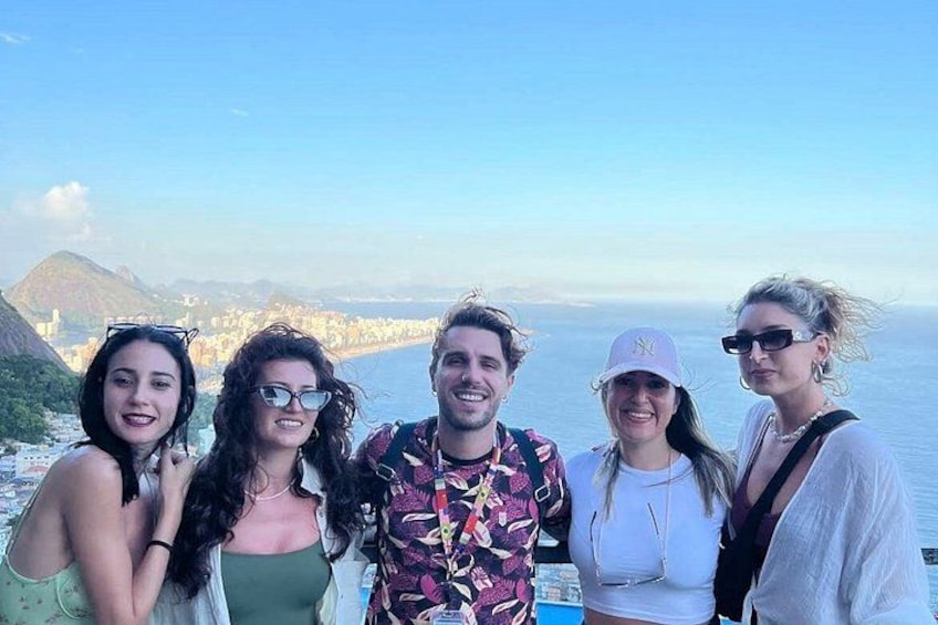 A group of people standing on a cliff overlooking a coastal city with mountains in the background. 3