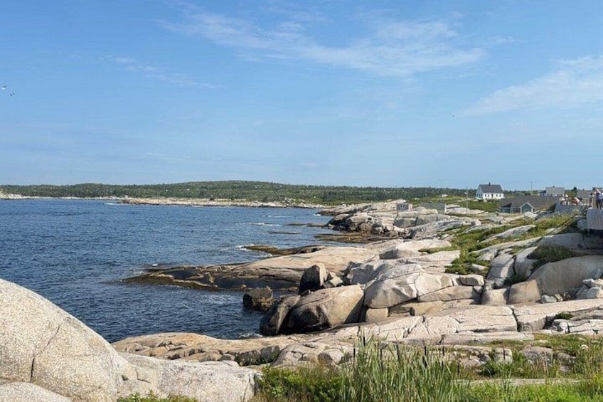 A rocky shoreline with large boulders, calm water, and a distant view of a coastline with houses. 2
