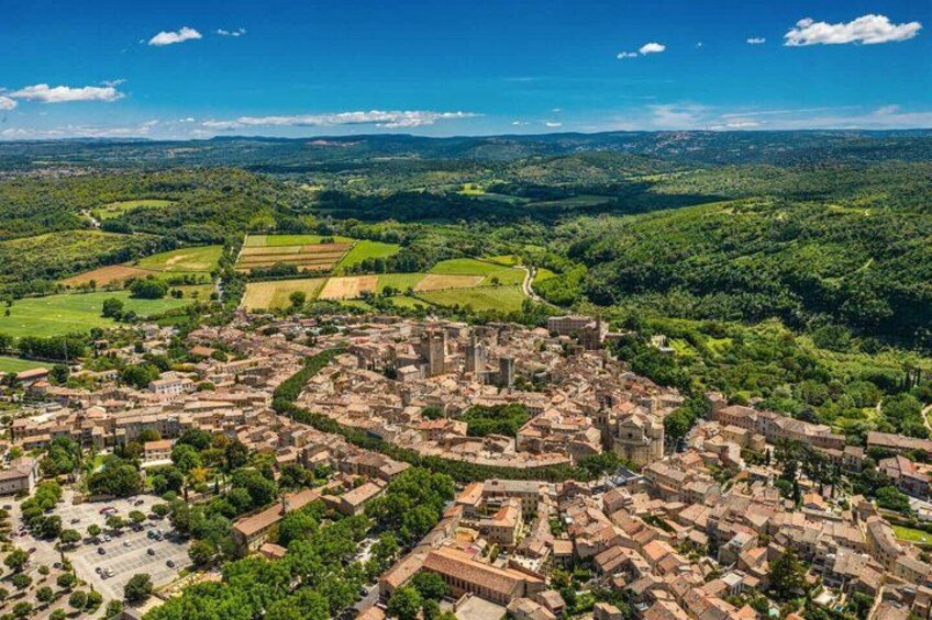 A historic town with dense medieval architecture, surrounded by lush green fields and rolling hills. 1