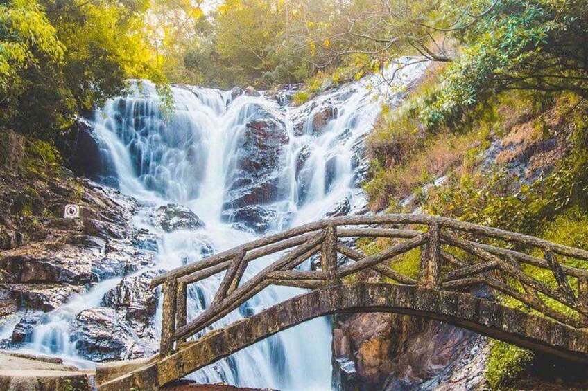 A waterfall cascading over rocks, a wooden bridge, and lush greenery. 2