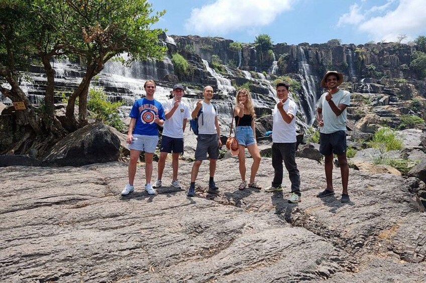A group of people standing on rocky terrain with a waterfall in the background. 5