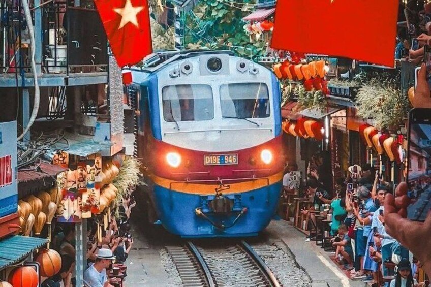 A train on tracks with people gathered around, a flag, and a building with a red roof. 3