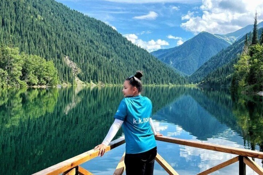 A person on a wooden dock overlooking a calm lake with forested mountains in the background. 2