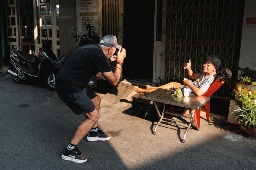 A man taking a photo of another man sitting at a table outdoors. 5