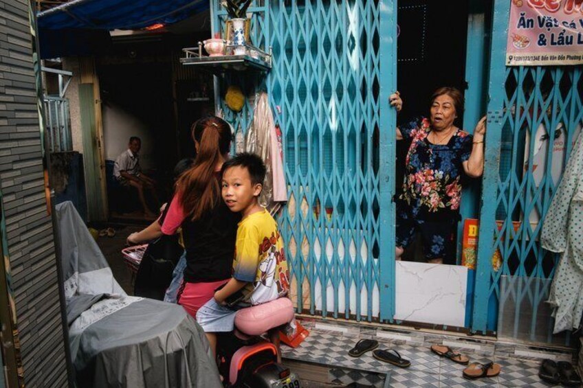 A narrow alleyway with a blue gate, a covered table, and a person sitting on a stool. 2