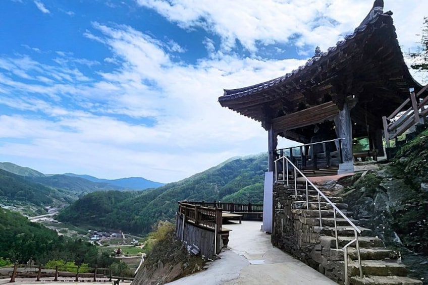 A traditional pavilion with a tiled roof, a stone staircase, and a view of a valley with mountains in the background. 3