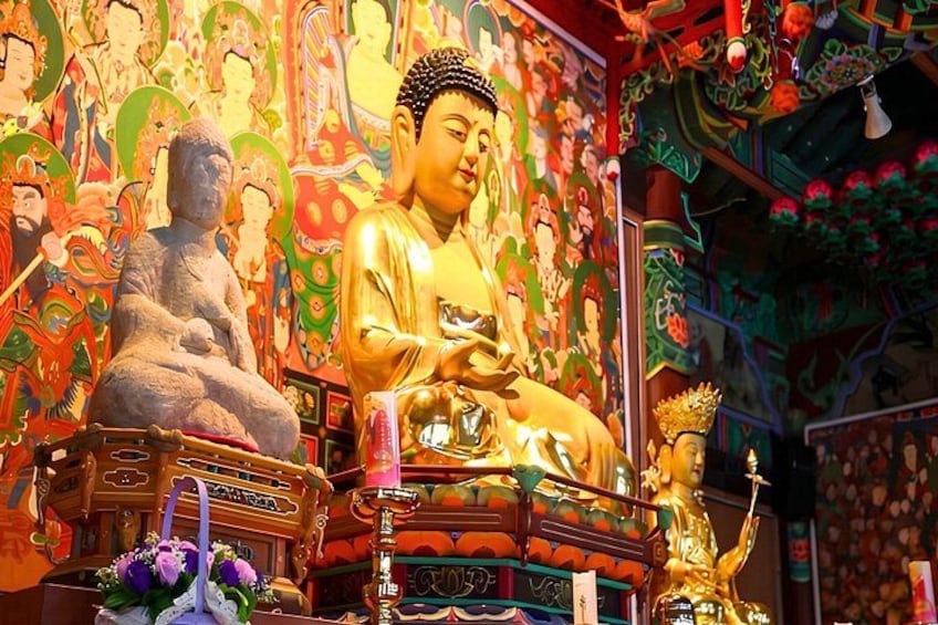 A large golden Buddha statue in a temple with colorful murals and smaller statues. 4