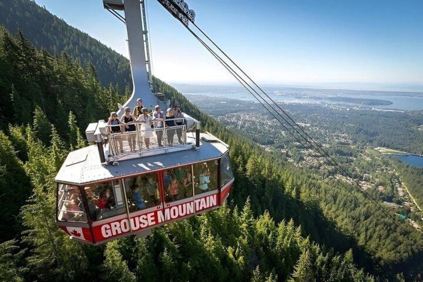 A cable car labeled 'Grouse Mountain' with passengers, suspended above a forested landscape. 1