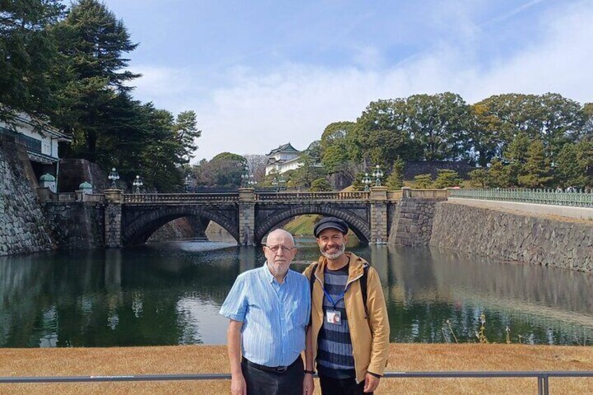Two people standing by a river with a stone bridge and traditional buildings in the background. 2