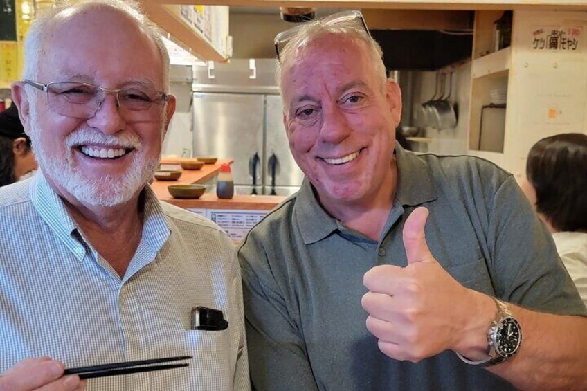Two men in a kitchen, one holding chopsticks and the other giving a thumbs-up. 3