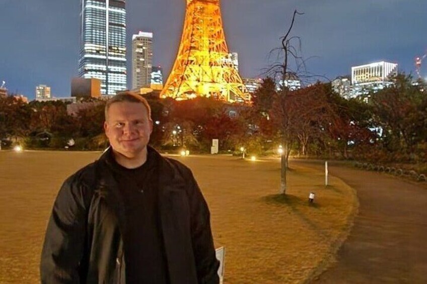 A person standing in a park with the Eiffel Tower illuminated in the background. 1