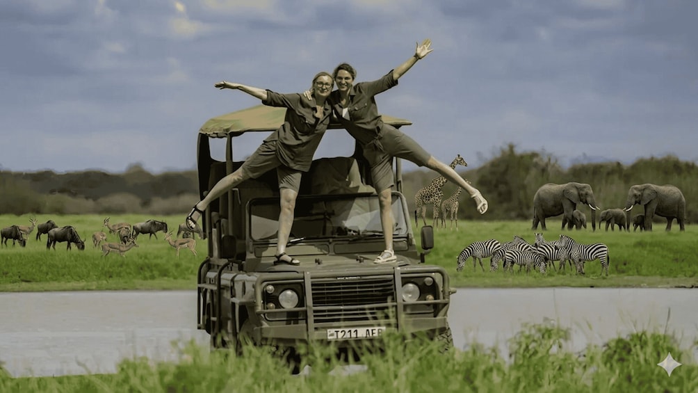 Two people on a safari vehicle with outstretched arms, surrounded by wildlife including zebras and elephants. 3