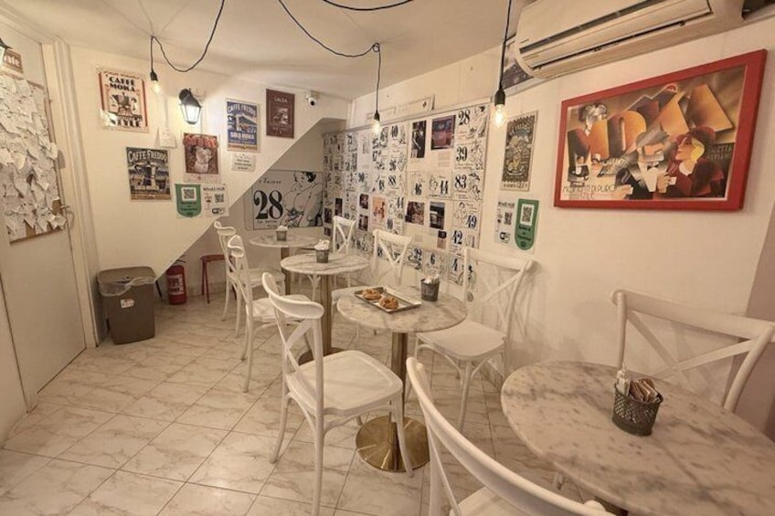 A café with white chairs and tables, decorated walls with posters and artwork, and a tiled floor. 2