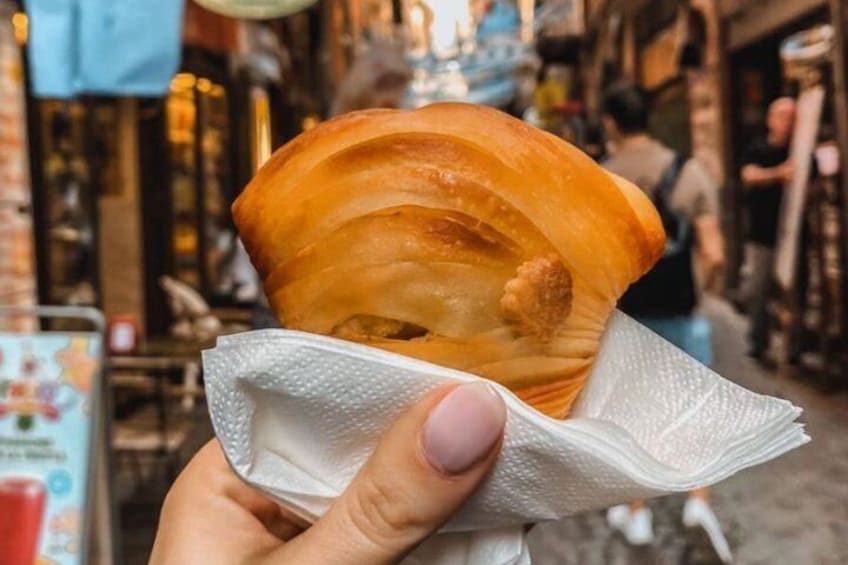 A person holding a fried food item, likely a doughnut, with a paper napkin. 1