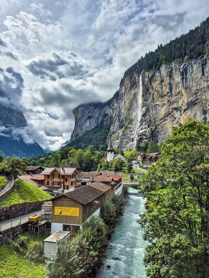 A river flowing through a village with a waterfall in the background and a mountain range. 3