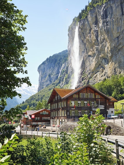 A wooden building with a Swiss flag, a waterfall, and a mountain backdrop. 2