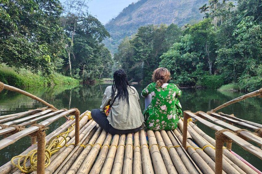 Two people sitting on a bamboo raft in a river surrounded by lush greenery. 3