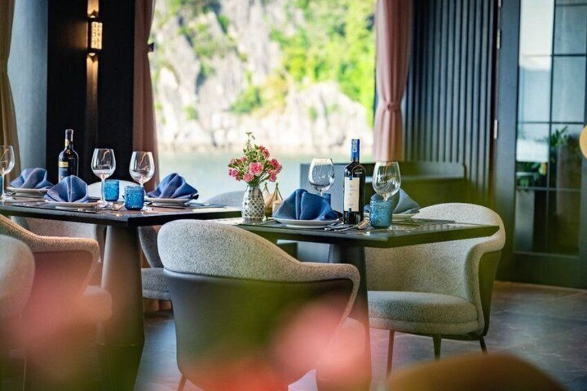 A restaurant table set with wine glasses, bottles, and a vase with flowers. 2