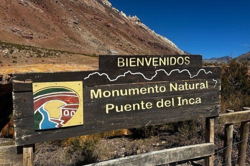 A wooden sign with 'BIENVENIDOS Monumento Natural Puente del Inca' and a colorful emblem. 3